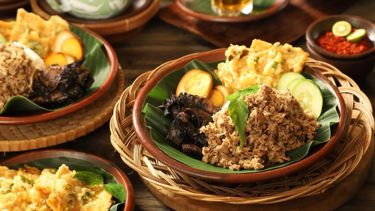Nasi Megono, traditional Javanese rice dish from Pekalongan, Central Java. It is steamed rice with Megono (stir-fried minced young jackfruit) as the main side dish; then added with Cumi Hitam (braised squid in its ink), Pindang Telur (braised egg in soy sauce) and Tempe Mendoan (fried tempeh in batter). The dish is plated on an earthenware plate lined with banana leaf. Served with Sambal (chili sauce) as the condiment. The Nasi Megono and Sambal are arranged on a table with another portion of Nasi Megono, extra portion of Tempe Mendoan and hot tea with the tea pot.