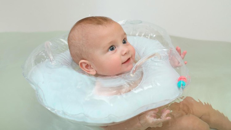 Pelampung leher bayi saat berenang Happy infant baby boy smiling while swimming in the bathtub with a rubber ring on his neck. Four month old child, close-up