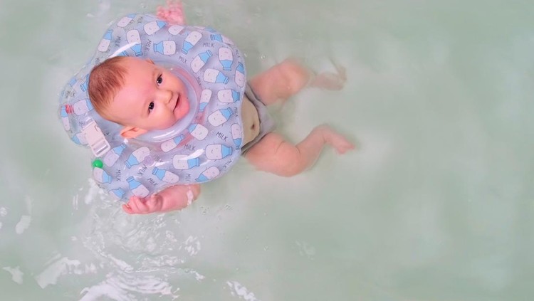 Pelampung leher bayi saat berenang Happy infant baby boy smiling while swimming in the bathtub with a rubber ring on his neck. Four month old child, close-up