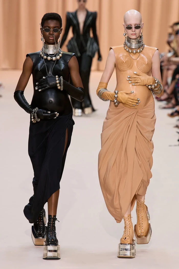 Salah satu yang mencuri perhatian adalah dress dengan ilusi serupa perut hamil. Aksesori turut jadi focal point seperti sunglasses dan anting hidung. Kedua aksesori tersebut juga turut dipakai Kim Kardashian dan North West yang berada di bangku penonton. Foto: Isidore Montag / Gorunway.com
