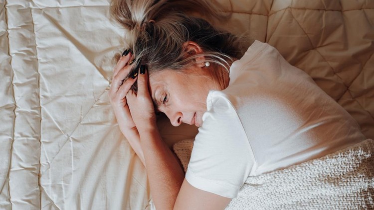 Top view depressed lonely upset caucasian adult woman lying on bed in bedroom. Portrait of middle-aged woman in crisis and with psychological problems. Mental health, melancholy, loneliness concept.