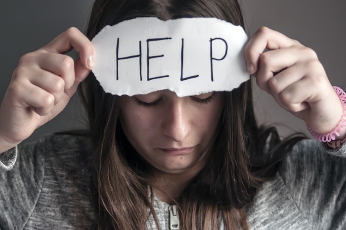 HELP, Teenager with help sign. girl holding a paper with the inscription. Homeless person with help sign. teenage girl in casual clothes holding sheet of paper. Girl holding sheet of paper with word HELP on grey wall background