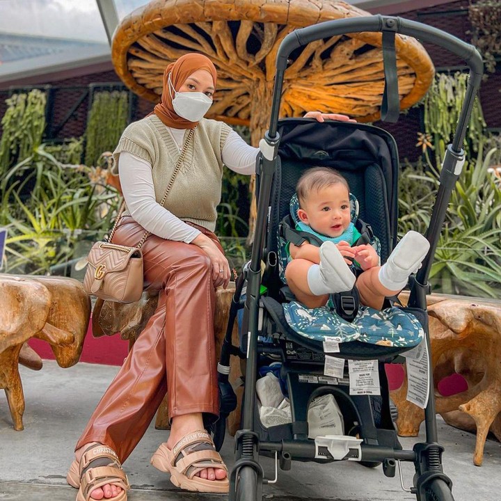 <p>Nah, kalau ini foto ketika berada di Gardens by the Bay. Nathalie mengenakan <em>outfit</em> bernuansa coklat. Sedangkan <em>baby</em> Adzam memakai baju hijau dan bergaya di atas stroller-nya. (Foto: Instagram @nathalieholscher)</p>