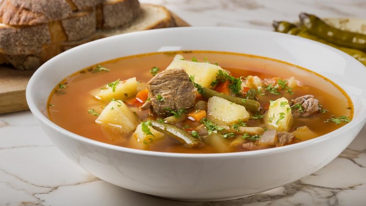 Resep Sop Daging Bowl of vegetable beef soup with sliced bread and hot chilli peppers in background
