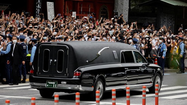 Ribuan warga memberikan penghormatan terakhir kepada mendiang Shinzo Abe, sebagian membungkuk ke arah mobil jenazah.