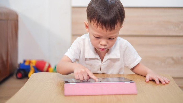 Confused aggressive Asian 2 - 3 years old toddler boy using tablet pc playing game, watching a video from tablet pc. Kids playing with tablet computer, Gadget-addicted children, pseudo-autism concept