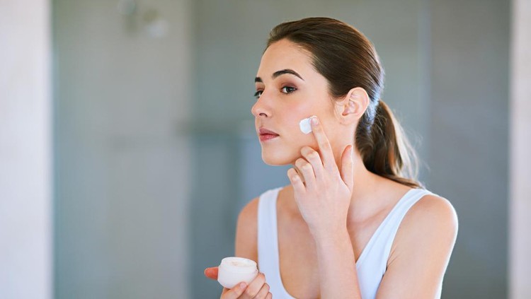 Ilustrasi Cara Memperbaiki Skin Barrier An attractive young woman applying cream to her face