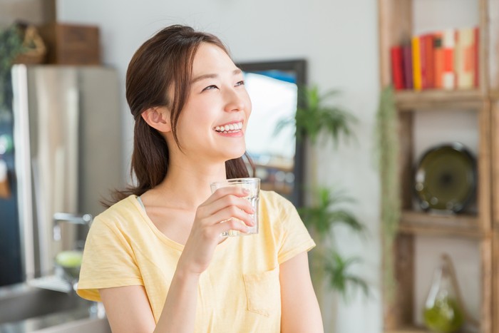 young attractive asian woman who drinks water in a kitchen