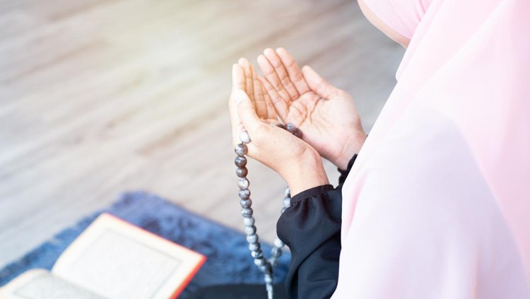 side of asian young beautiful muslim woman pray with beads and read quran sit on carpet mat with meditation in mosque.