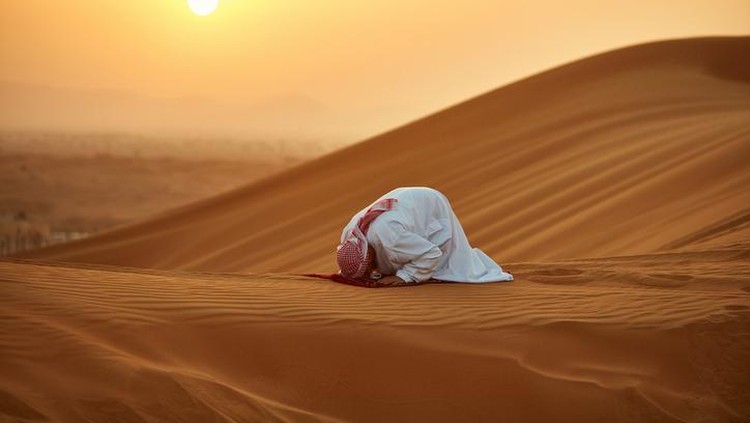 ilustrasi zuhud Arab man praying on mat in desert. Male is in traditional wear. He is kneeling on sand.