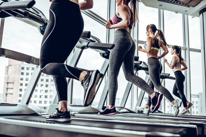 Running together. Side view of young beautiful women looking away while running on treadmill at gym.