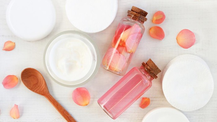 Tonic and cream, cotton pads, bottles, fresh pink flowers, wooden table preparation background.