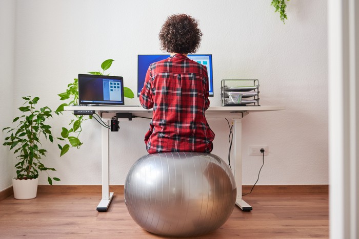 Back view of a woman teleworking sitting on a fitball in front of her desk