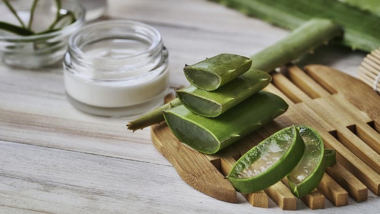 Aloe vera slices and moisturizer on a wooden table. Beauty treatment concepts