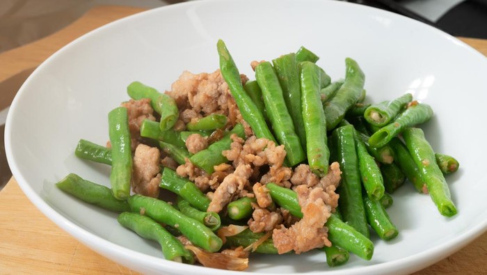 Close up stir-fried cowpeas or black-eyed beans with minced pork with garlic and soy sauce, food in the white disk on cutting board in the kitchen, Asian homemade menu.