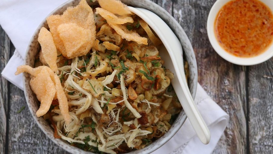 Ilustrasi Resep Bubur Suro A popular Peranakan breakfast and fast food dish in Indonesia, consists of rice porridge with toppings of shredded chicken, sliced Chinese croissant, fried shallot, chopped celery leaves, and crisp crackers. Accompanied with chili sauce. Typically an inexpensive, street food dish, it is now served in a fancy ceramic bowl with Chinese-style, ceramic soup spoon tucked on the upper right hand side. A casually-folded white linen napkin underlines the bowl. The meal is served on an unpolished, rustic wooden table. The image was taken outdoor in the morning and used sunlight as the natural lighting source.
