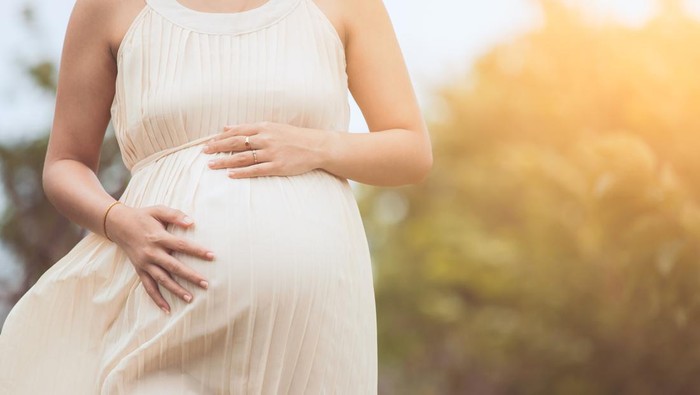 Pregnant woman touching her big belly and walking in the park relaxing in outside