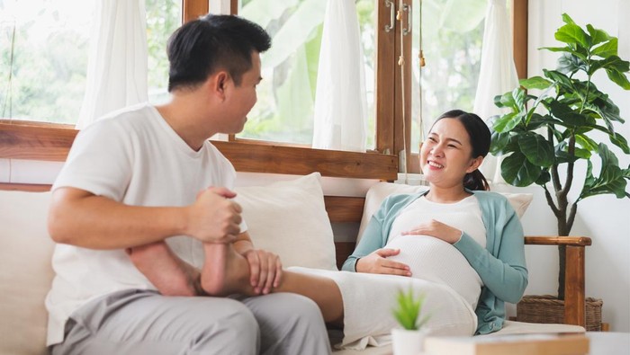 Asian young husband massaging pregnant wife feet at home, happy family