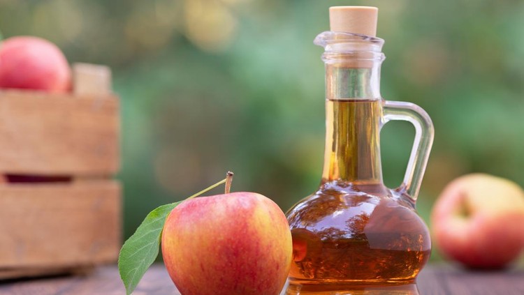 apple vinegar in glass pitcher and ripe fresh apples on wooden table outdoors