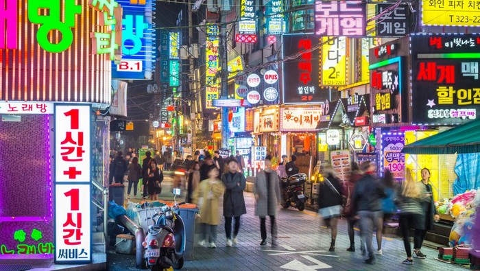 Crowds of people walking through the colourfully illuminated neon night streets of Sinchon, Seoul, South Korea.