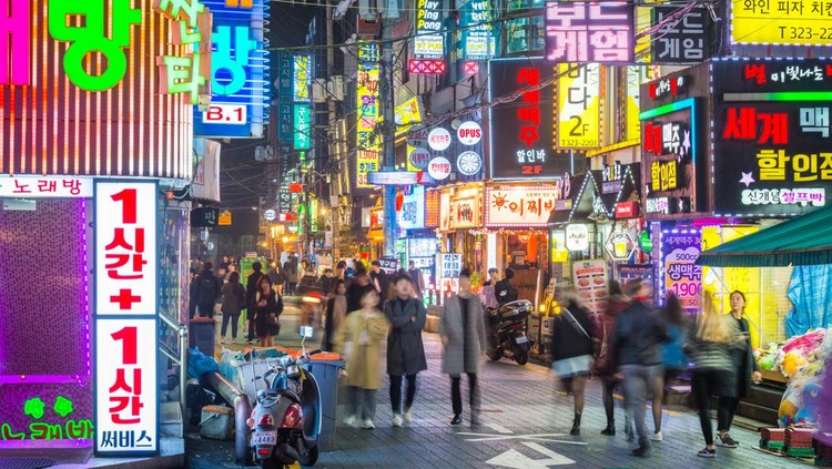 Crowds of people walking through the colourfully illuminated neon night streets of Sinchon, Seoul, South Korea.