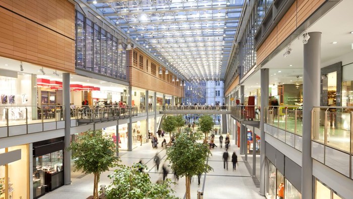 Image taken inside a shopping mall. There are lots of people walking around going to stores, buying things and consuming food and beverages. There are two floors with shops and boutiques. The ceiling is glass. The architecture is very modern and new and the general feel of the images is bright, clean, safe and positive.