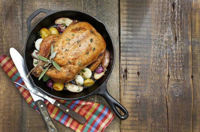 A overhead view of a roast chicken on a rustic wood table top.