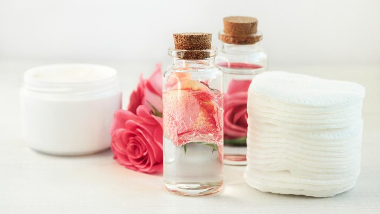 Glass bottle with attar bubbles and rose petals, cotton pads. Healing homemade skincare moisture toni