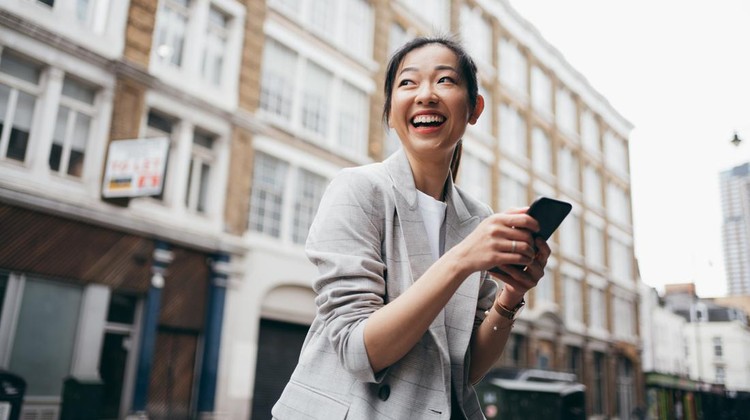 Ilustrasi Kata-kata Bijak Singkat Asian business woman looking far away while using her smartphone on the street of London.