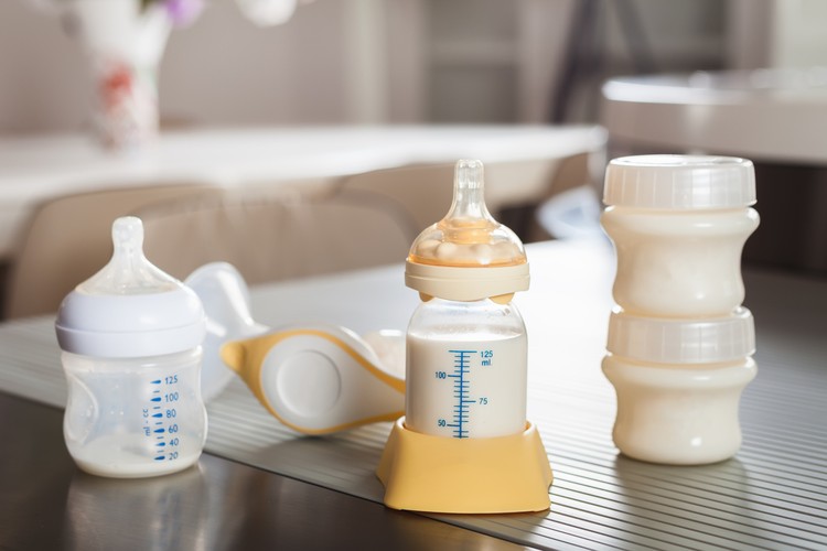 Baby bottle with milk and manual breast pump. A lot of full bottles with breast milk on the background. Mother's milk - the most healthy food for newborn