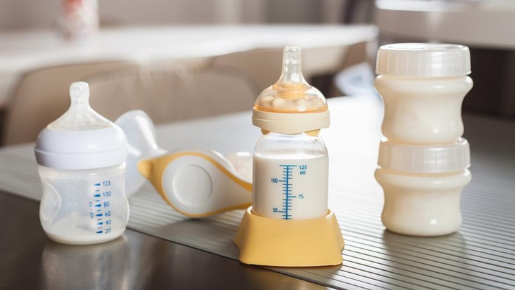 Baby bottle with milk and manual breast pump. A lot of full bottles with breast milk on the background. Mother's milk - the most healthy food for newborn