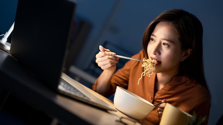 Ilustrasi wanita makan mi instan depan laptop