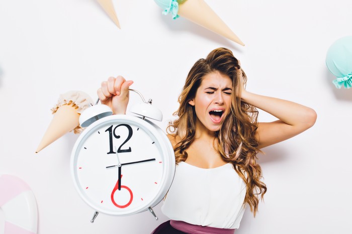 Upset girl scream with eyes closed touching head in panic and holding big white clock. Portrait of distressed young woman in white tank-top, shout during posing on background decorated with ice cream.