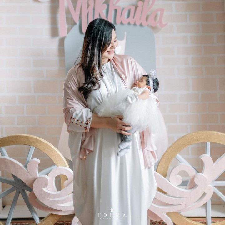<p>Saat tasyakuran aqiqah, baby Mikhaila tampil cantik dalam balutan gaun putih ditambah bando berwarna serupa. Ia begitu nyenyak dalam gendongan Bundanya. (Foto: Instagram @eriskarien)</p>