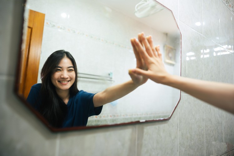 1276364966 Young adult smile asian woman practice self talk conversation in the morning in bathroom at home. Hand hi-touch at mirror. Healthy lifestyle after wake up concept.