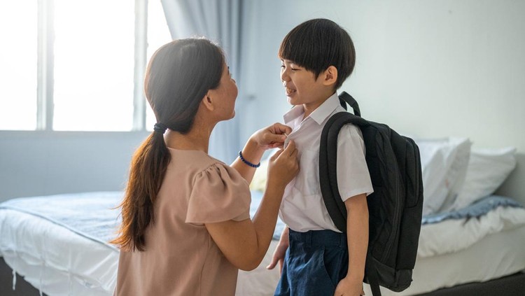 An Asian mother getting her son ready for school at home.