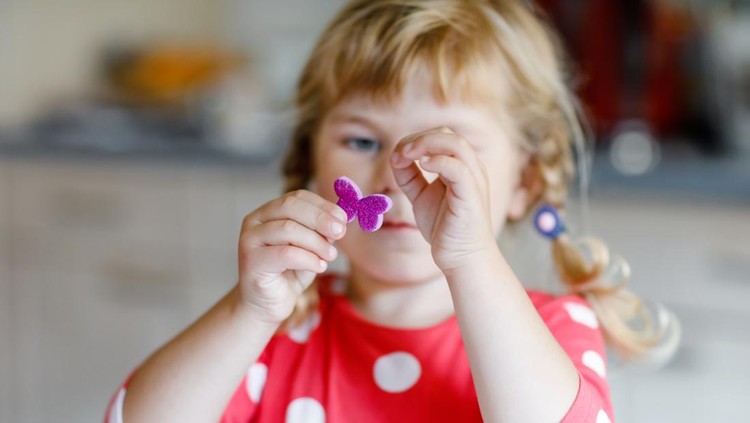 Little toddler girl playing with different colorful stickers and painting flowers. Concept of activity of children during pandemic corona virus quarantine. Child learning colors with parents at home.