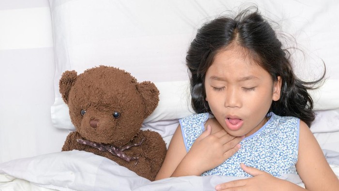 Little girl is coughing and sore throat lying on bed with toy bear, Health care concept