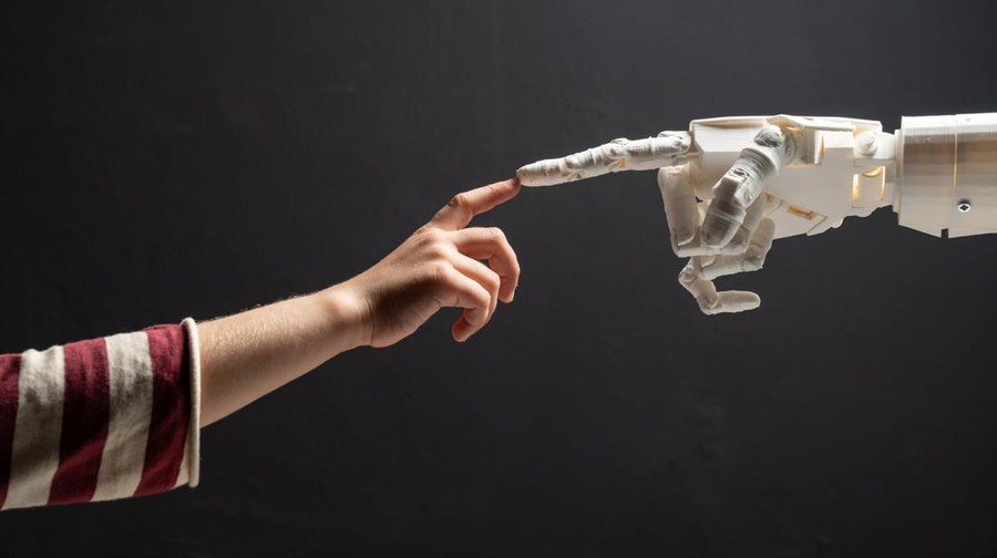 Humanoid robot finger and children finger meets in front of blackboard. Shot in studio with a full frame mirrorless camera.