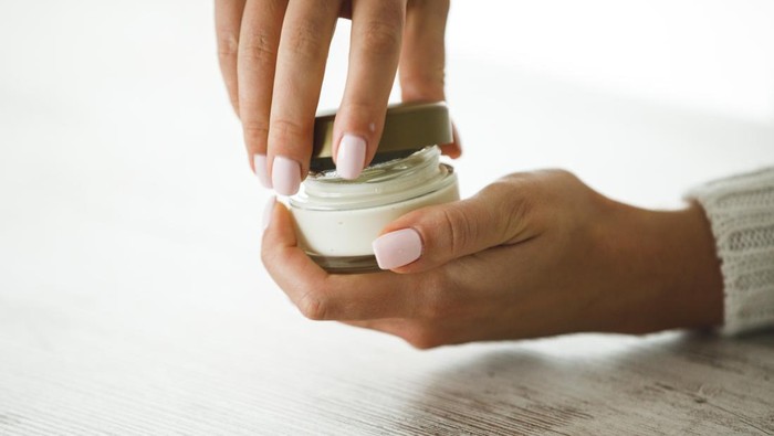 Close up of female hands opening a small round jar of cream by twisting the lid before using it to moisturize skin.