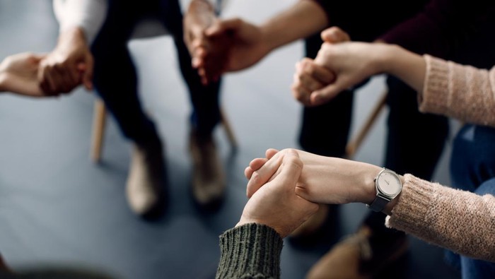 Close-up of people holding hands while sitting in a circle during group therapy.