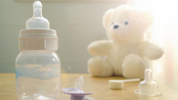 Baby bottle, pacifier and a baby's toy on a wooden table