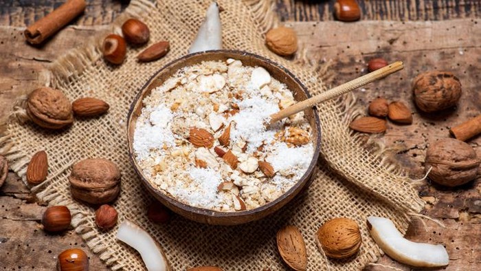 Oatmeal cereals with grated coconut and nuts in a bowl of coconut shell tabletop view