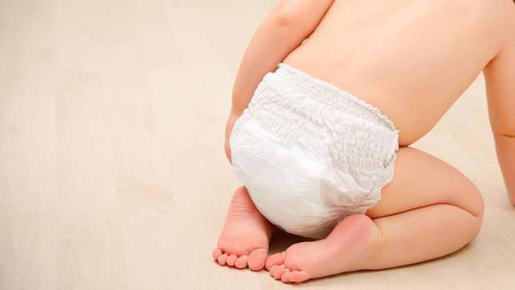 Baby crawling on wooden floor in diaper pants. Back view