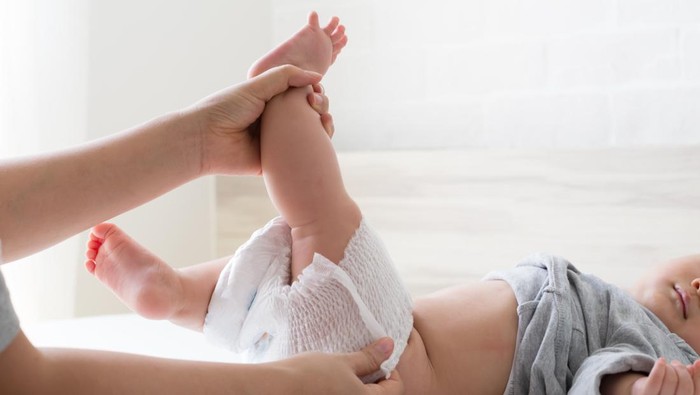 Mother changing diaper for her son on white bed in bedroom
