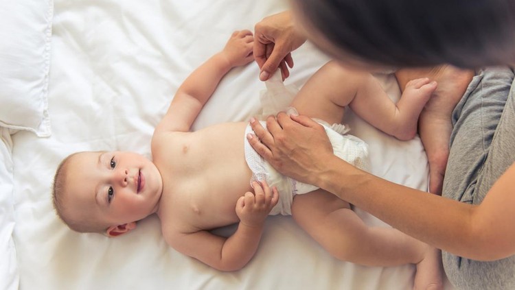 Rekomendasi Popok Bayi Newborn Top view of charming naked little baby looking at his mommy and smiling while she is changing him nappies
