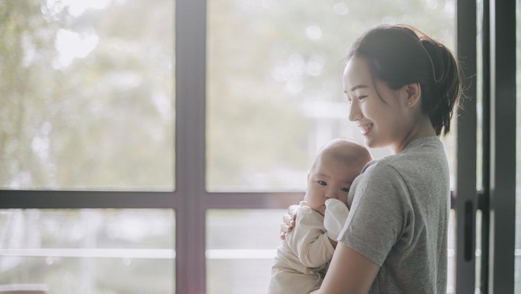 Asian Chinese Mother carrying her baby boy from crib in the morning bonding time with backlit sunlight