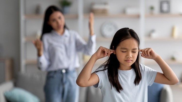 Family argument concept. Offended asian girl covering ears, not wanting to listen to her mother's scolding, selective focus. Young woman having fight with her child, quarelling at home