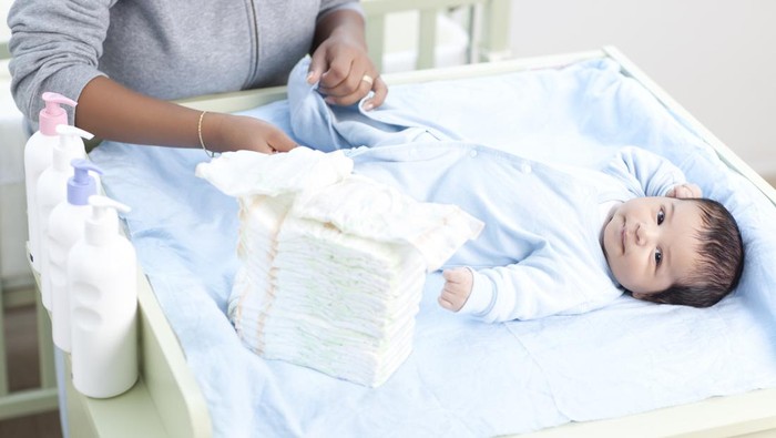 Hands of mother changing disposable diapers (pampers) to her baby.