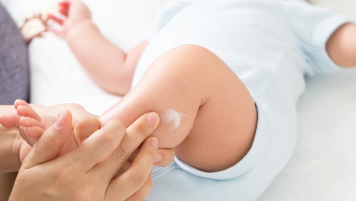 Mother is applying cream to the baby boy which helps to maintain skin leg hydration, Skincare and moisturizing cream concept
